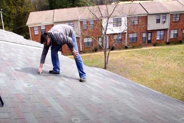 Roof worker inspecting roof marking the damaged portion with chalk